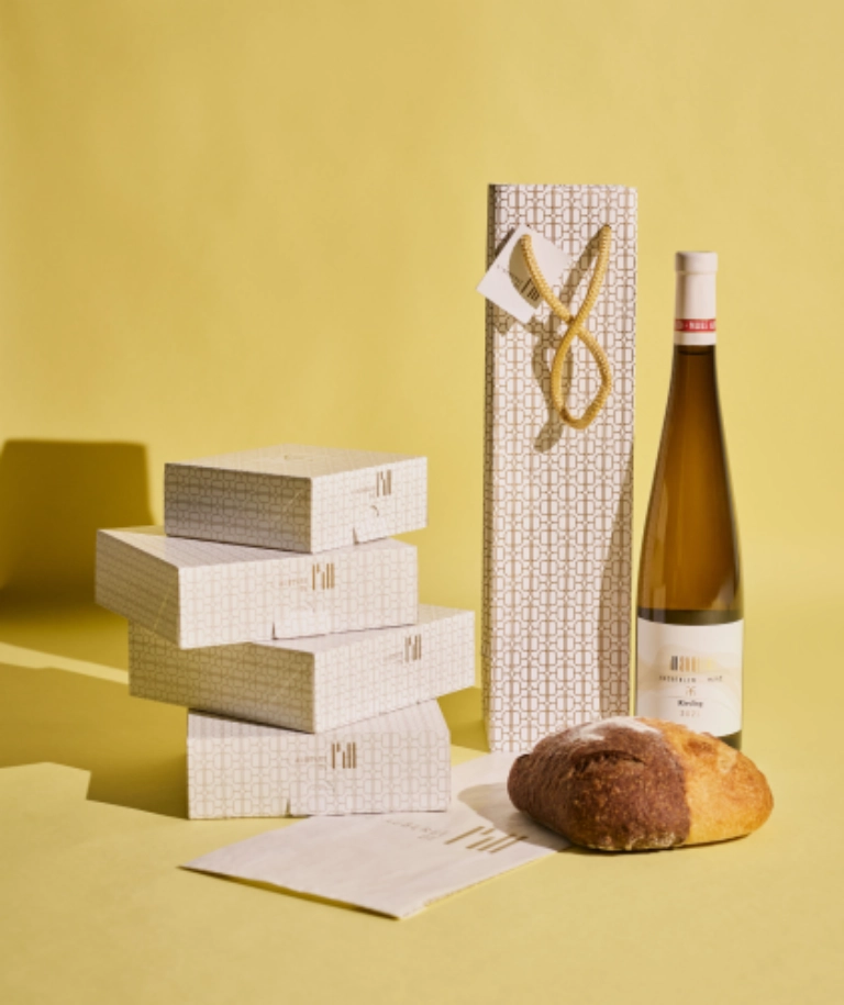 Emballages sur-mesure pour l’Auberge de l’Ill, incluant un sac pour les bouteilles de vin, une boîte pour les pâtisseries et un sac en papier pour le pain, conçus par Schneider Packaging.