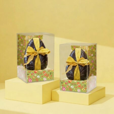 Boîte moulage transparente personnalisée avec socle personnalisable, mettant en valeur des moules en chocolat tels que poules, œufs et autres créations gourmandes, pour une présentation élégante.
