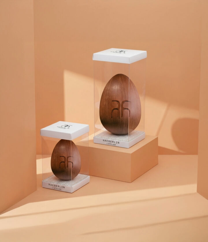 Boîte moulage transparente personnalisée avec socle personnalisable, mettant en valeur des moules en chocolat tels que poules, œufs et autres créations gourmandes, pour une présentation élégante.